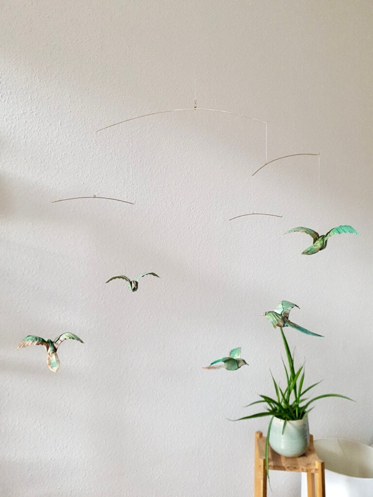 A hanging mobile with green origami birds and a green plant