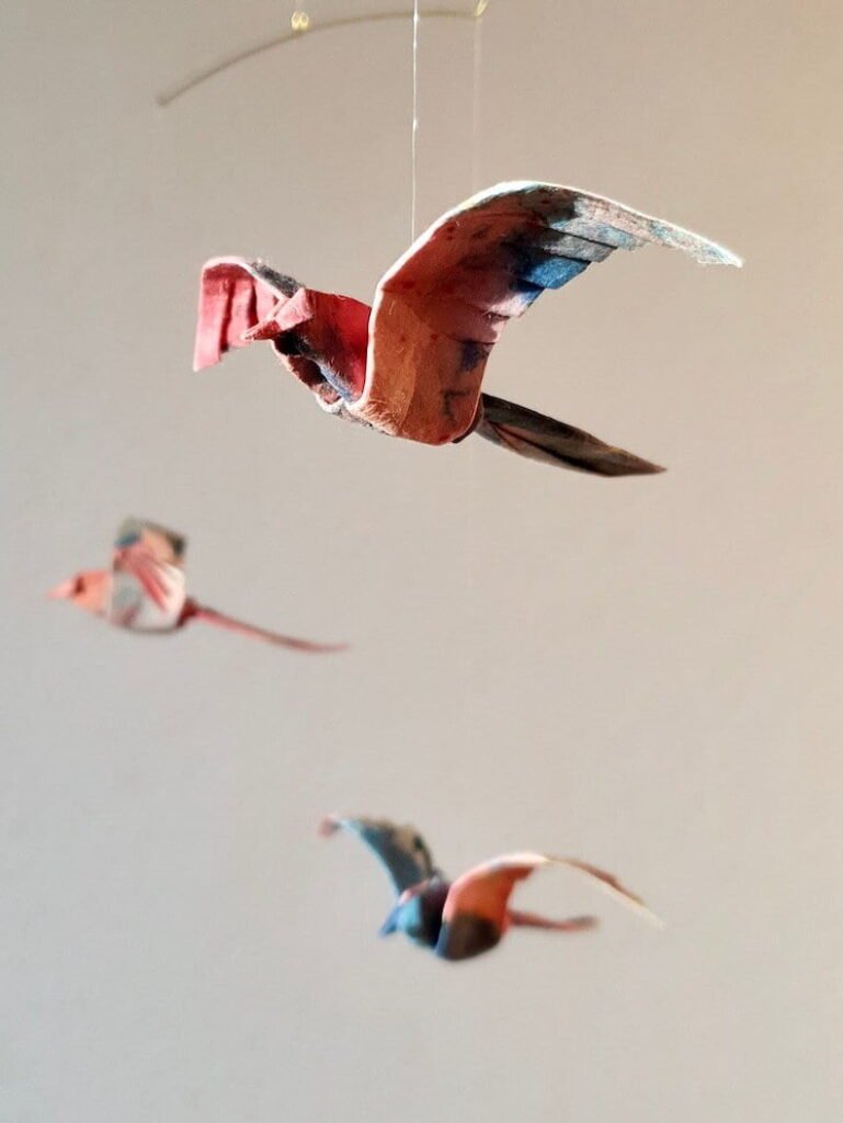 A hanging mobile with 3 blue and pink origami birds in sunlight