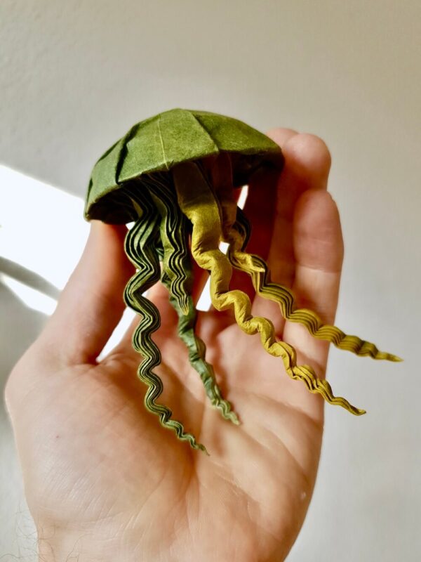 A hand holding a green origami jellyfish