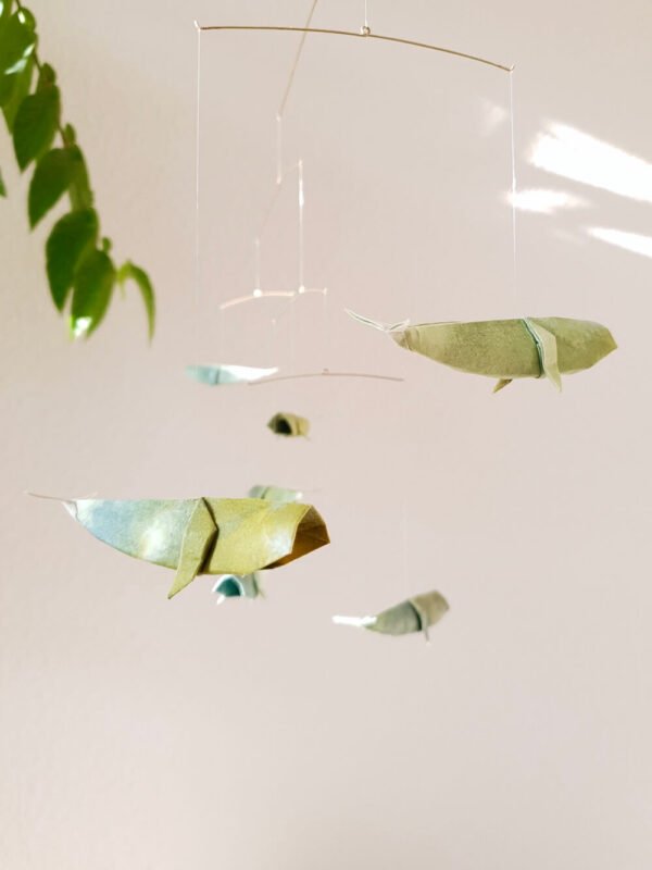 A hanging mobile with origami whales in hues of blue and green.