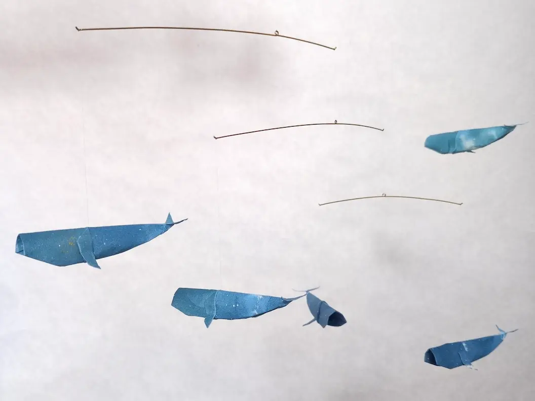 A hanging mobile with 5 blue kirigami whales