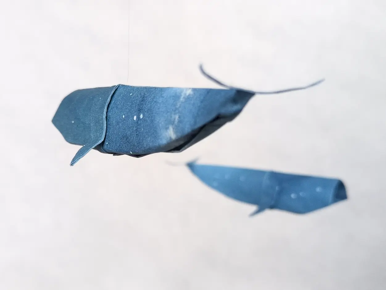 A hanging mobile with blue kirigami whales